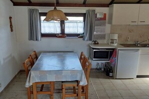 Ein Essbereich mit Tisch und Stühlen, einem Fenster mit Vorhängen, einer Mikrowelle, einem Kühlschrank und einem Kalender an der Wand.
