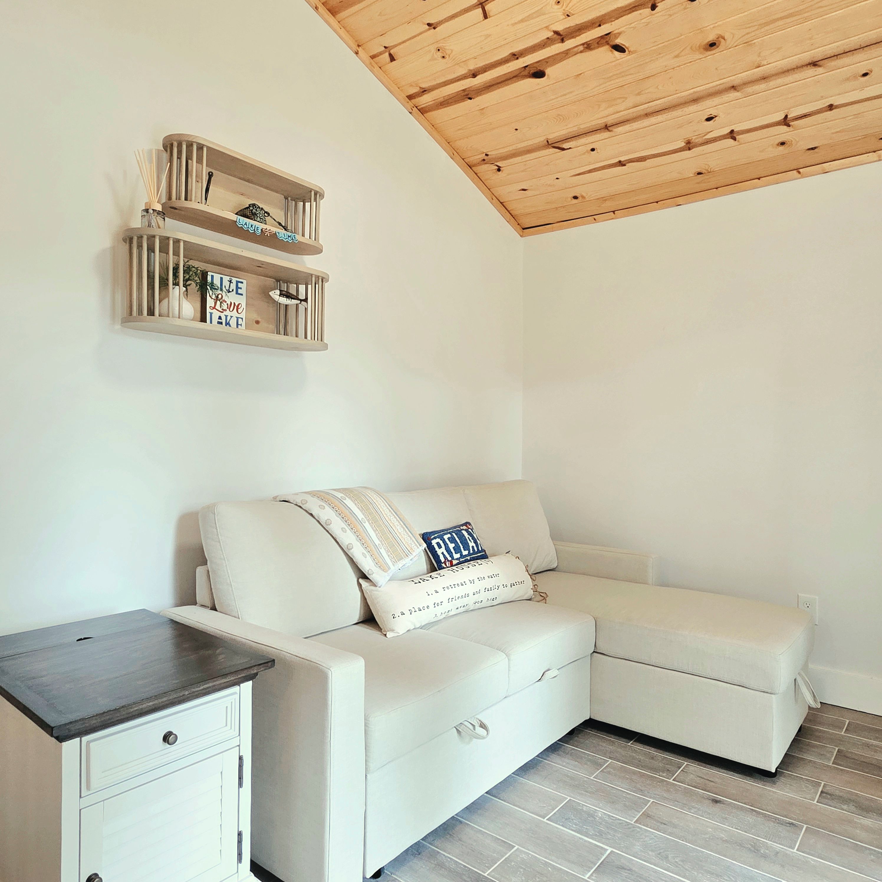 Ein Eckzimmer mit einem weißen Sofa, einem kleinen Nachttisch und einer Holzbalkendecke.