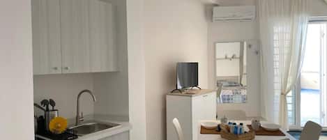 Cocina compacta con pileta, pequeño refrigerador y comedor con mesa y sillas.