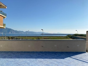 A terrace with a view of the sea and mountains, a tiled floor, and a low wall. - Casa Emy (Torre Annunziata)