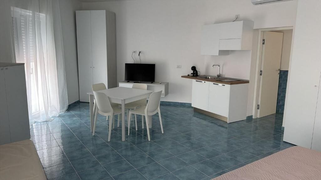 A modern kitchen with white cabinets, a dining table with chairs, and a television.