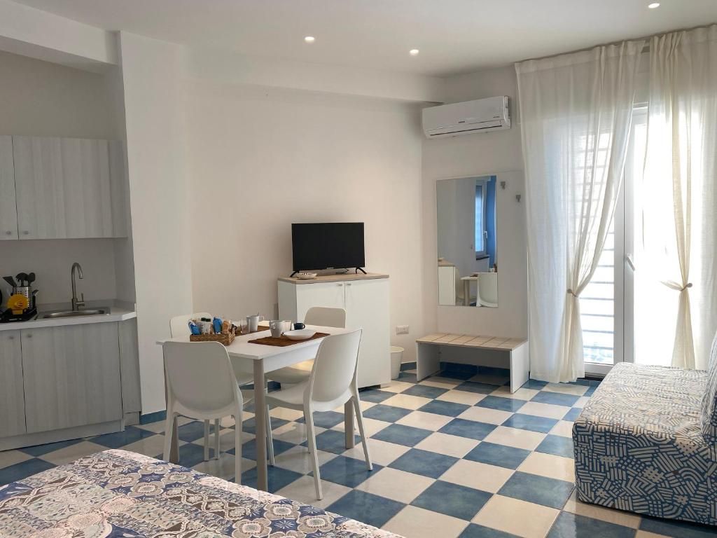 Una camera d'albergo con pavimento a scacchi, un letto, una TV, un'area pranzo e angolo cottura.