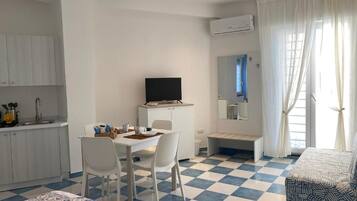 Una camera d'albergo con pavimento a scacchi, un letto, una TV, un'area pranzo e angolo cottura.