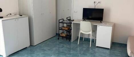 Una habitación con cama, escritorio, silla, televisor y armario.