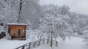 A wooden cabin with a snow-covered roof, surrounded by snow-laden trees and a wooden fence.