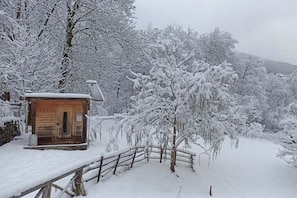 A wooden cabin with a snow-covered roof, surrounded by snow-laden trees and a wooden fence.