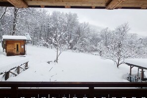 A wooden cabin with a snow-covered roof, surrounded by snow-laden trees and a wooden deck.