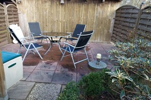 Een terras met een ronde tafel en vier stoelen, een kleine prullenbak en een plant in een pot.