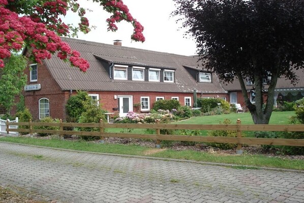 Een gebouw van baksteen met twee verdiepingen, een geplaveid oprit en een houten hek.