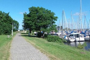 Ein gepflasterter Weg entlang eines Gewässers mit mehreren vertäuten Booten.