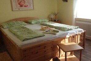 Een houten bed met een bankje, een nachtkastje met een lamp en een lijst met een foto aan de muur.
