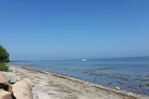 Een kustpad met heldere lucht, een boot in de verte en een rotsachtige kustlijn.