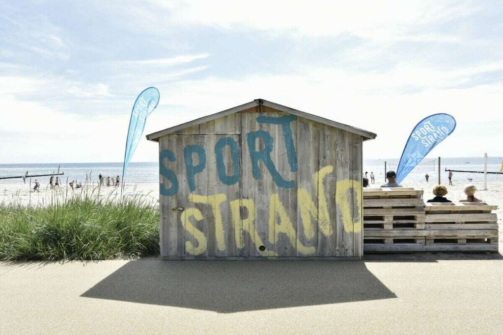 A wooden structure with graffiti that reads 'SPORT STRAND' and two blue flags with the same text.
