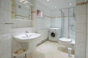 Een badkamer met een wastafel, toilet, wasmachine en een douchecabine met glazen wanden.