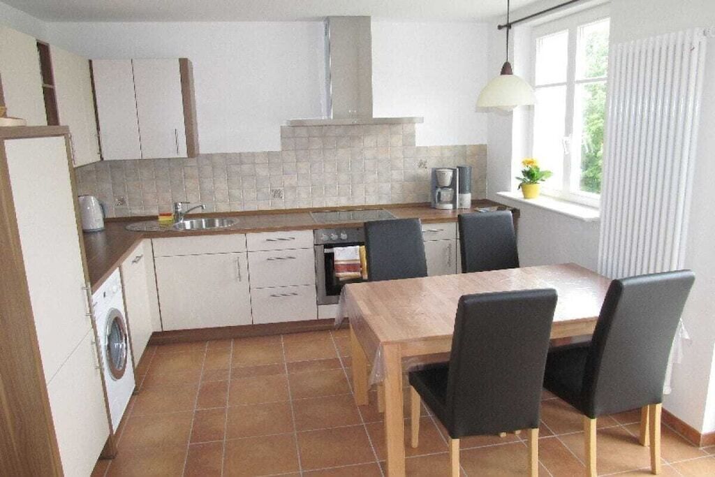 A compact kitchen with a dining area, a washing machine, and a window with a view.