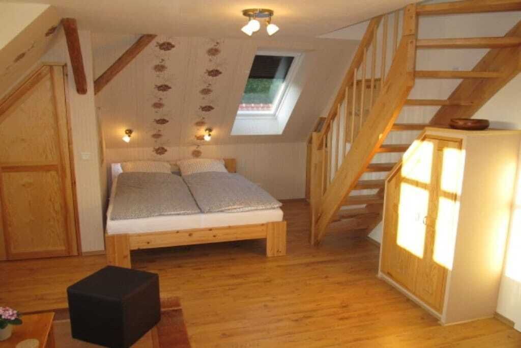 Ein Schlafzimmer im Loft-Stil mit einer Holztreppe, einem Oberlicht und einem Bett mit Kissen.