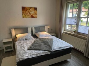 Un dormitorio con cama, mesitas de noche, una ventana con vistas y un cuadro en la pared.