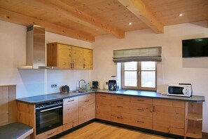A modern kitchen with wooden cabinets, a built-in oven, a microwave, and a window with blinds. - Holiday apartment with 3 bedrooms (Lenggries)