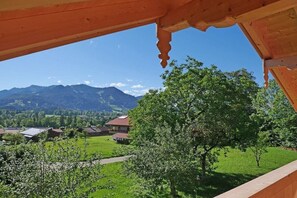 Un balcó de fusta amb vista a un paisatge de muntanya, un arbre i un camí que condueix a cases.