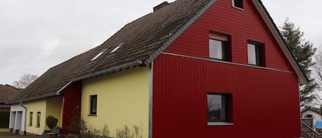 Un edificio rojo y amarillo con techo inclinado, un pequeño porche y una ventana visible.