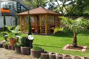 Un belvédère en bois, surmonté d’un toit en tuiles, entouré d’une pelouse bien entretenue et de plantes en pot.