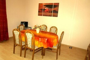 A dining area with a round table, six chairs, a vase with flowers, and a painting on the wall.