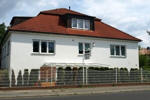 A two-story house with a red-tiled roof, white exterior walls, and a white fence.
