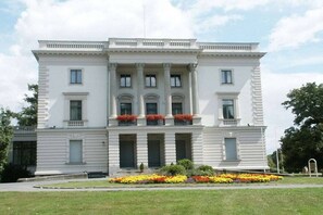 Un grand bâtiment blanc à deux étages, doté d’une façade symétrique, de nombreuses fenêtres et d’une entrée centrale flanquée de colonnes.