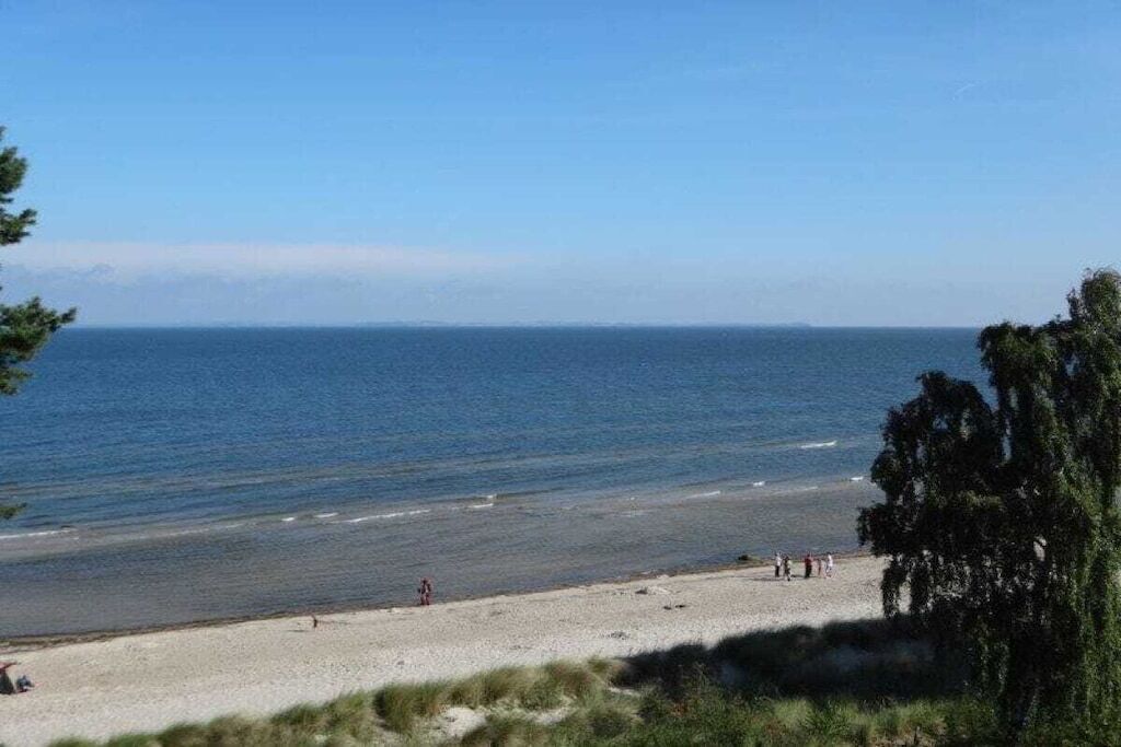 Une plage avec un ciel dégagé, une eau calme et quelques personnes.