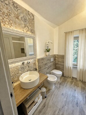 A modern bathroom with a large mirror, two sinks, a toilet, and a potted orchid. - Vrbo Property (Arezzo)