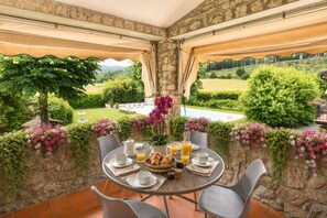 A dining area with a table set for breakfast, overlooking a pool and lush garden. - Vrbo Property (Arezzo)