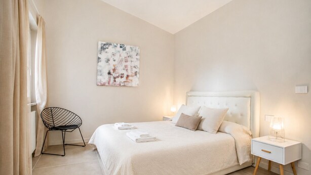 Une chambre à coucher moderne avec un grand lit, une chaise, une table de chevet avec une lampe et un tableau au mur.