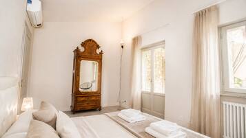 A bedroom with a bed, a wooden dresser, a mirror, a radiator, and a window with curtains.