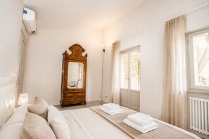 A bedroom with a bed, a wooden dresser, a mirror, a radiator, and a window with curtains. - Vrbo Property (Arezzo)
