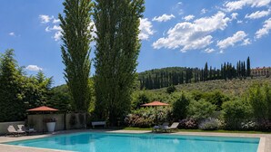 Une piscine rectangulaire, agrémentée de deux chaises longues et de parasols, entourée d’un jardin où poussent différentes plantes et fleurs.