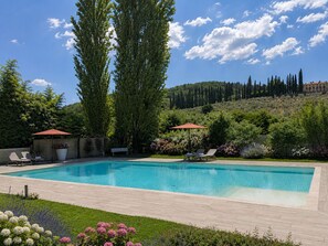A rectangular swimming pool with two lounge chairs and umbrellas, surrounded by a garden with various plants and flowers. - Apartment in a Tuscan villa with a park and pool for relaxing in nature (Arezzo)