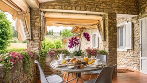 Une terrasse en pierre avec une table ronde mise pour le petit-déjeuner, entourée de chaises.