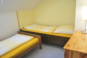 Une petite chambre, de taille modeste, avec deux lits simples et une table de chevet en bois.