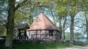 Ein traditionelles Gebäude im Tudor-Stil mit einem kegelförmigen Dach, umgeben von Bäumen und einer Steinmauer.