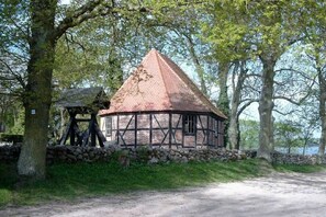 Un bâtiment traditionnel de style Tudor, doté d’un toit conique, entouré d’arbres et d’un mur de pierre.