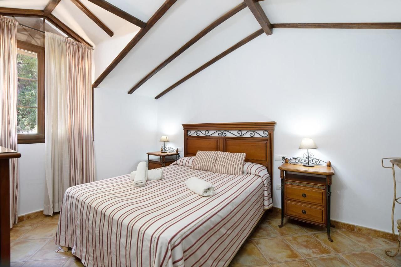 Een slaapkamer met een houten hoofdbord, een bed met gestreept beddengoed, twee nachtkastjes met lampen en een raam met gordijnen.