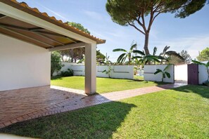 A covered patio area with a brick pathway leading to a white wall with a gate. - Mi Pasión I        . (Chiclana de la Frontera.)