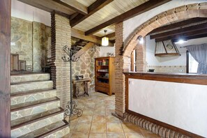 Ein rustikales Interieur mit Steinwänden, Holzbalken, einer Treppe, einem Bücherregal und einer Wanduhr.