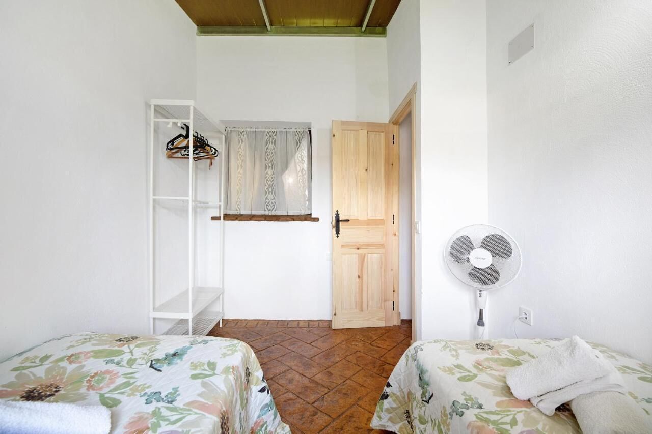 Ein Schlafzimmer mit zwei Betten, einem Kleiderschrank, einem Ventilator und einer Tür zu einem weiteren Raum.