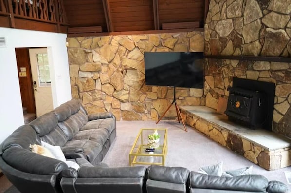 Una sala de estar con una pared de piedra, un televisor de pantalla plana montado en ella, una chimenea y un sofá de cuero.