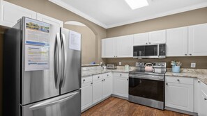 A modern kitchen with stainless steel appliances, white cabinetry, and a wooden floor. - 832 Cypress Bend - Barefoot Resort Rentals (North Myrtle Beach)