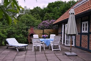Une terrasse avec une table et des chaises, un fauteuil de relaxation et un parasol.