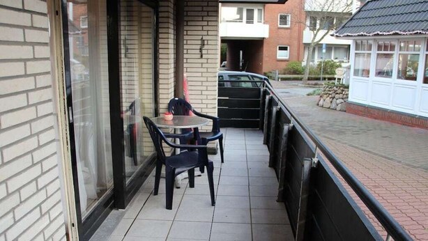 Un balcó amb una taula, cadires, una porta de vidre i vista al carrer.