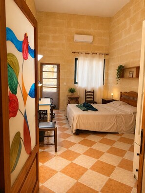 A bedroom with a bed, a desk, a chair, a window with curtains, and a wall-mounted air conditioner.