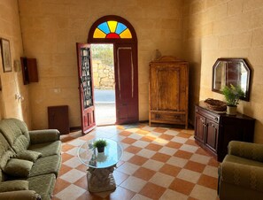 A room with a checkered floor, a glass-top coffee table with a plant, a wooden cabinet, and a door with a stained glass window.